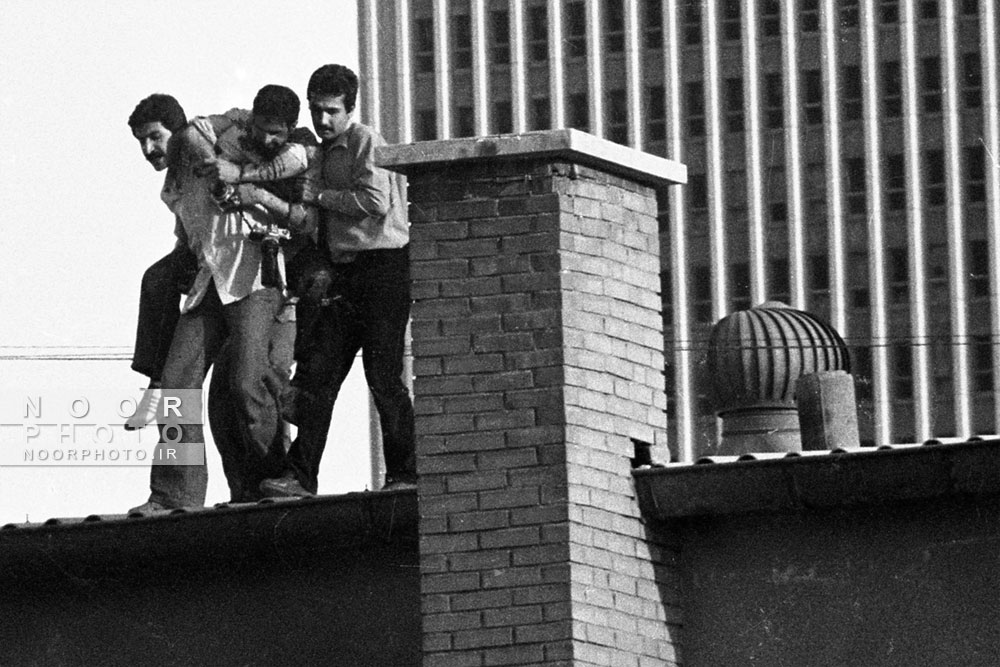 یک عکاس ایرانی با دو دوربین عکاسی بر روی پشت بام پس از اصابت پنج گلوله توسط نیروهای امنیتی با یک تک تیرانداز اشتباه گرفته بودند مجروح شد این عکاس در حال پوشش ناآرامی های خیابانی بین مجاهدین خلق و گروه های حزب الله، طرفدار  دولت جمهوری اسلامی بود. تهران، ایران 16/06/1980. 